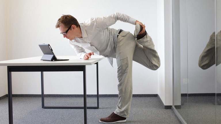 man standing and stretching while looking at his tablet on the desk
