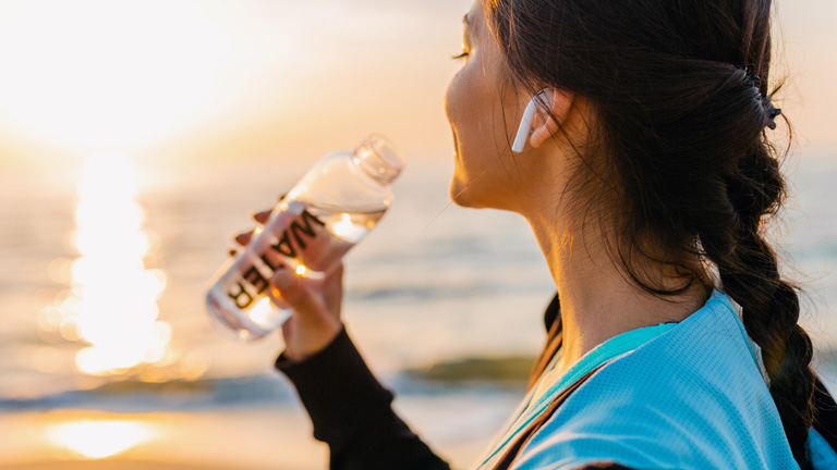 ワイヤレスヘッドフォンをして海辺で一休みする、運動中の女性