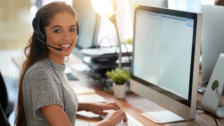 Young woman helping a customer on the phone and using her computer