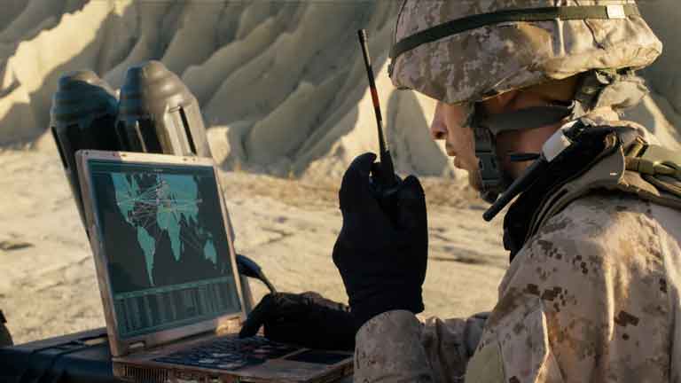 Soldier out in the field using a laptop and calling in stats 