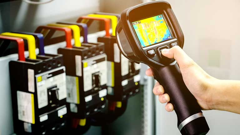 A handheld thermal imaging device shows the heat coming off high-voltage cables