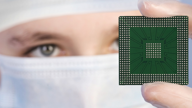 lab tech in cleanroom gear holding up micrchip